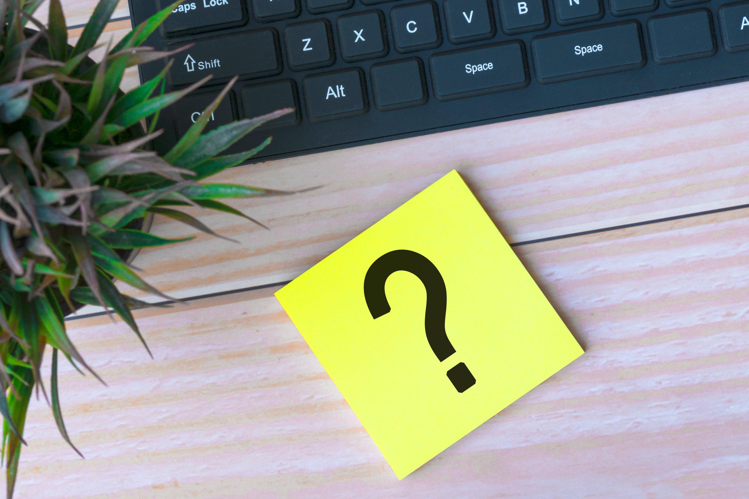 Question mark on adhesive note on wooden desk with keyboard